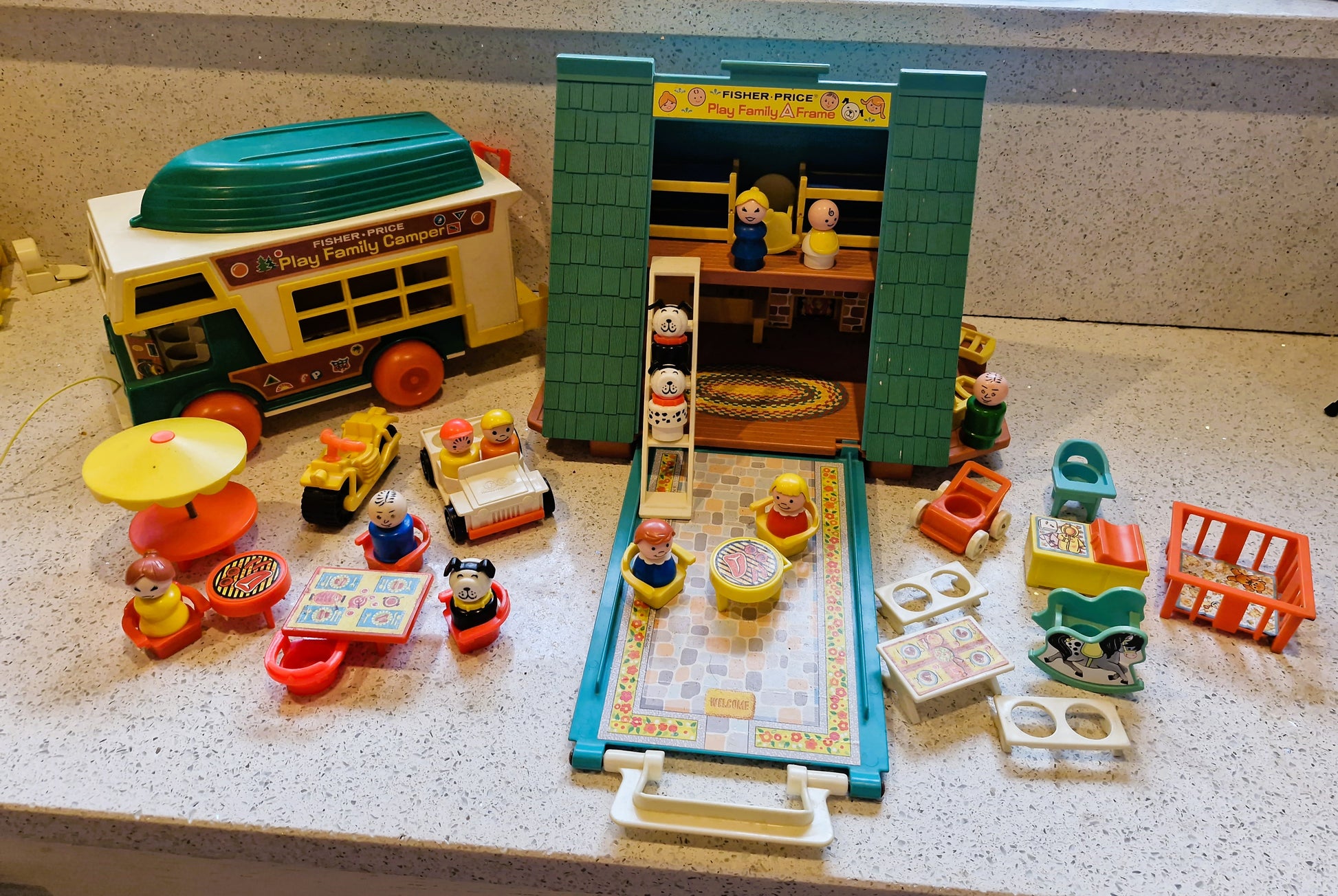 Vintage toy set with a camper, furniture, and people on a speckled countertop.