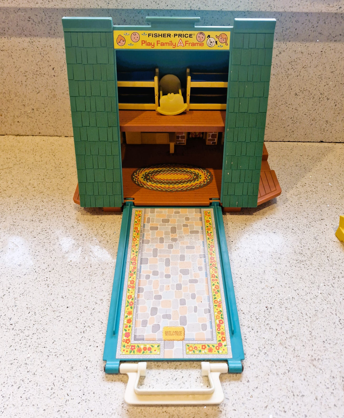Fisher-Price playset with a green and blue structure on a speckled countertop.