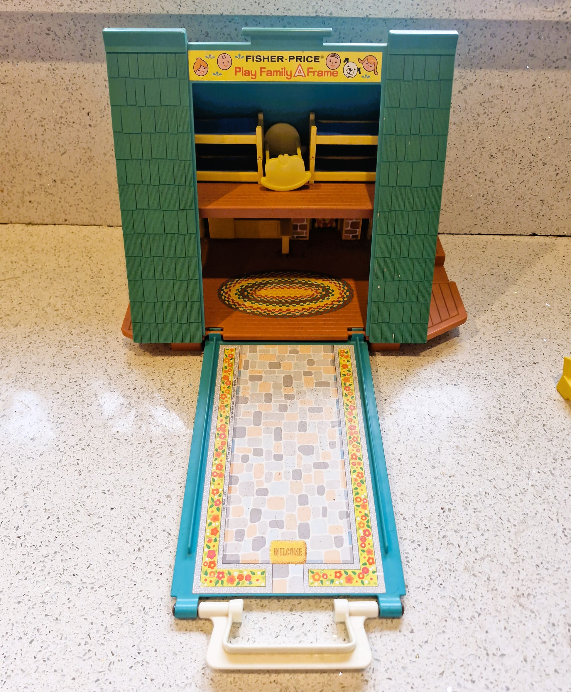 Fisher-Price playset with a green and blue structure on a speckled countertop.