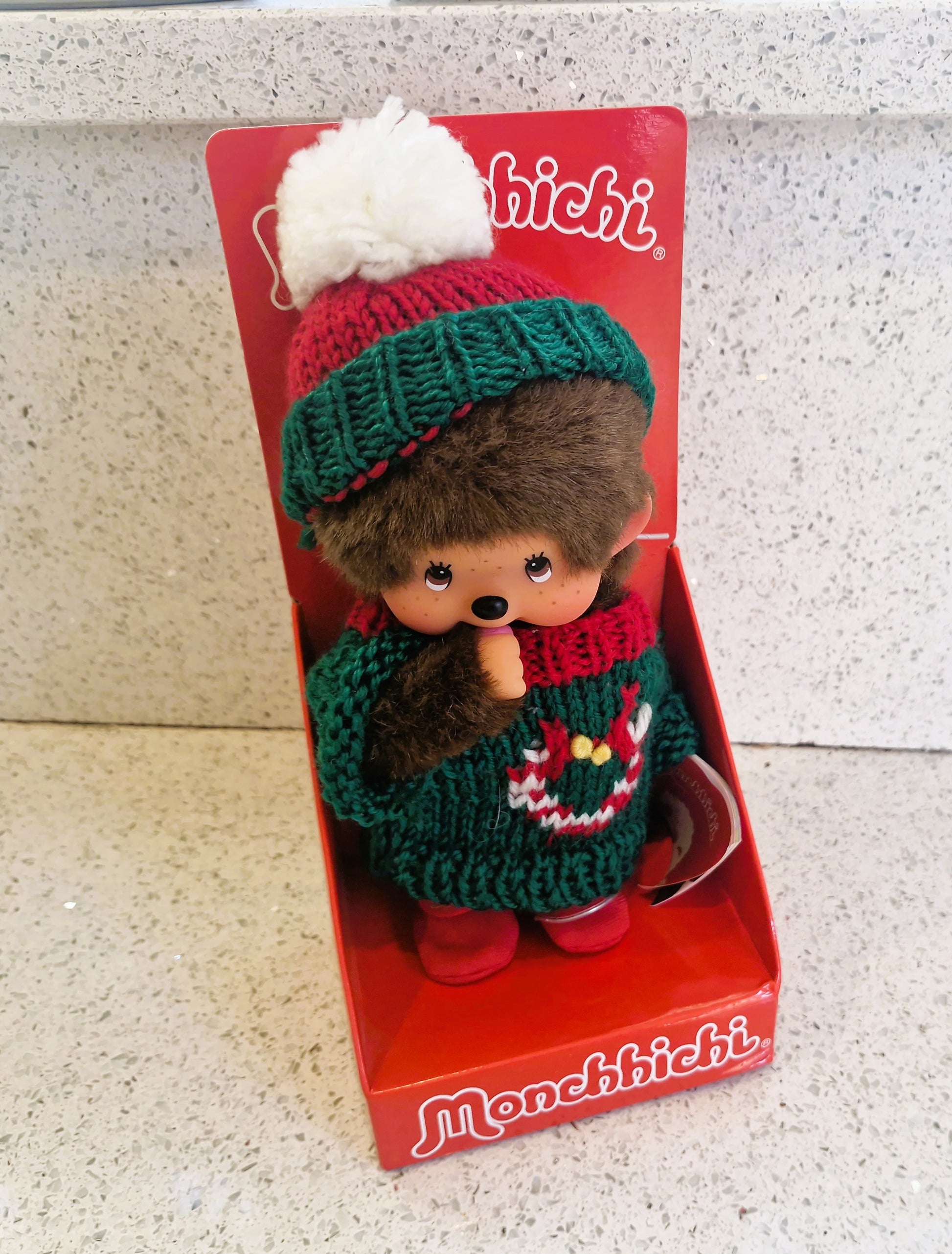 Monchhichi toy in a red box with a textured surface background